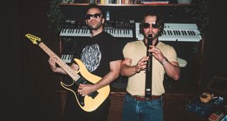 Cobra Kai composers Zach Robinson [left] and Leo Birenberg in the studio. Pictured in front of a bank of keyboards, Robinson plays an Ibanez RG550, while Birenberg plays woodwind.