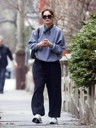 A photo of Katie Holmes accessorizing her gray crewneck sweatshirt with a navy neckerchief, black pants, and white sneakers.