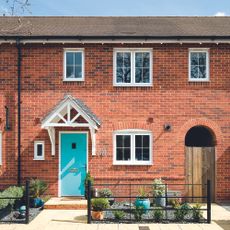 red brick wall house with roof white window plants and blue door 