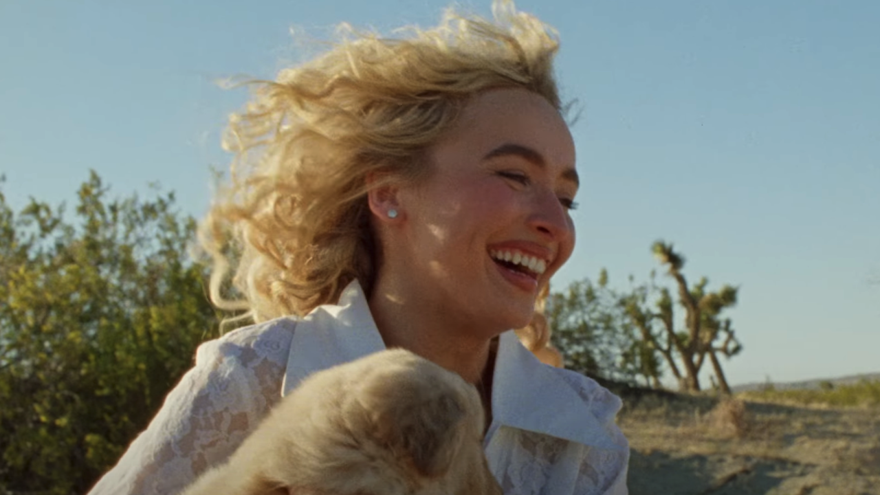 Sabrina Carpenter running while smiling with a puppy in her arms in Manchild music video