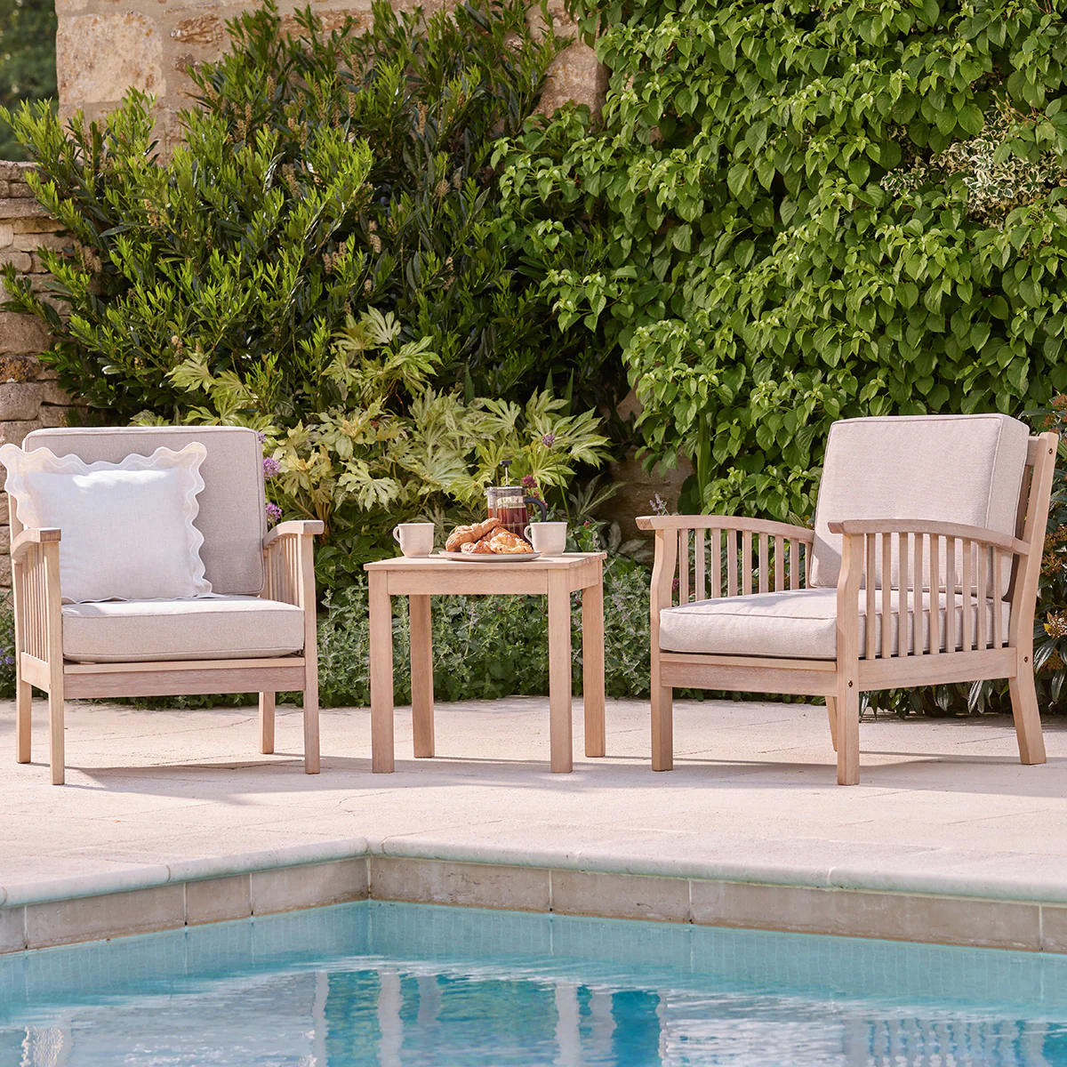 two armchairs next to a pool with greenery behind
