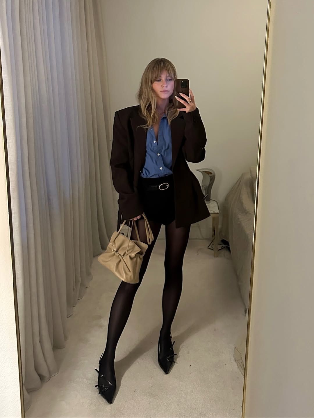 Jeanette Madsen takes a mirror selfie wearing the Prada Dada bag in beige with a black short suits, blue shirt and black heels