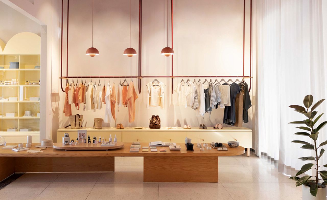 Lagalá shop IMOX, clothing hanging on copper rails suspended from ceiling with copper lamps above, wooden table and pot plant