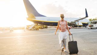 woman with suitcase walking towards plane