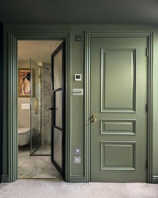 A hallway with olive green walls and an open door into a bathroom