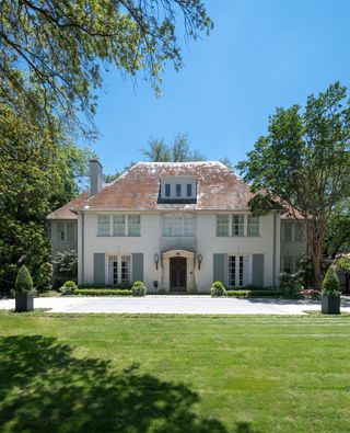 Exterior of 1920s French style home with slate roof and wings either side of symmetrical facade