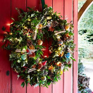 Christmas wreath with lights mistletoe and pine cones hanging on red door