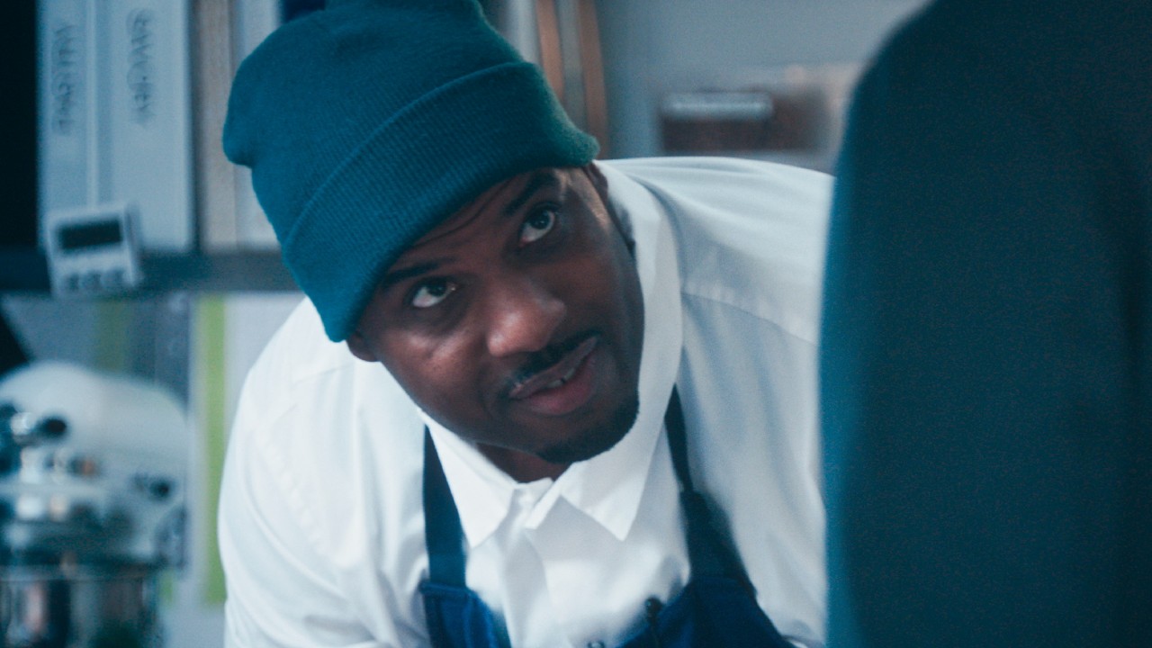 Lionel Boyce as Marcus leaning down and looking up in the kitchen of The Bear. 