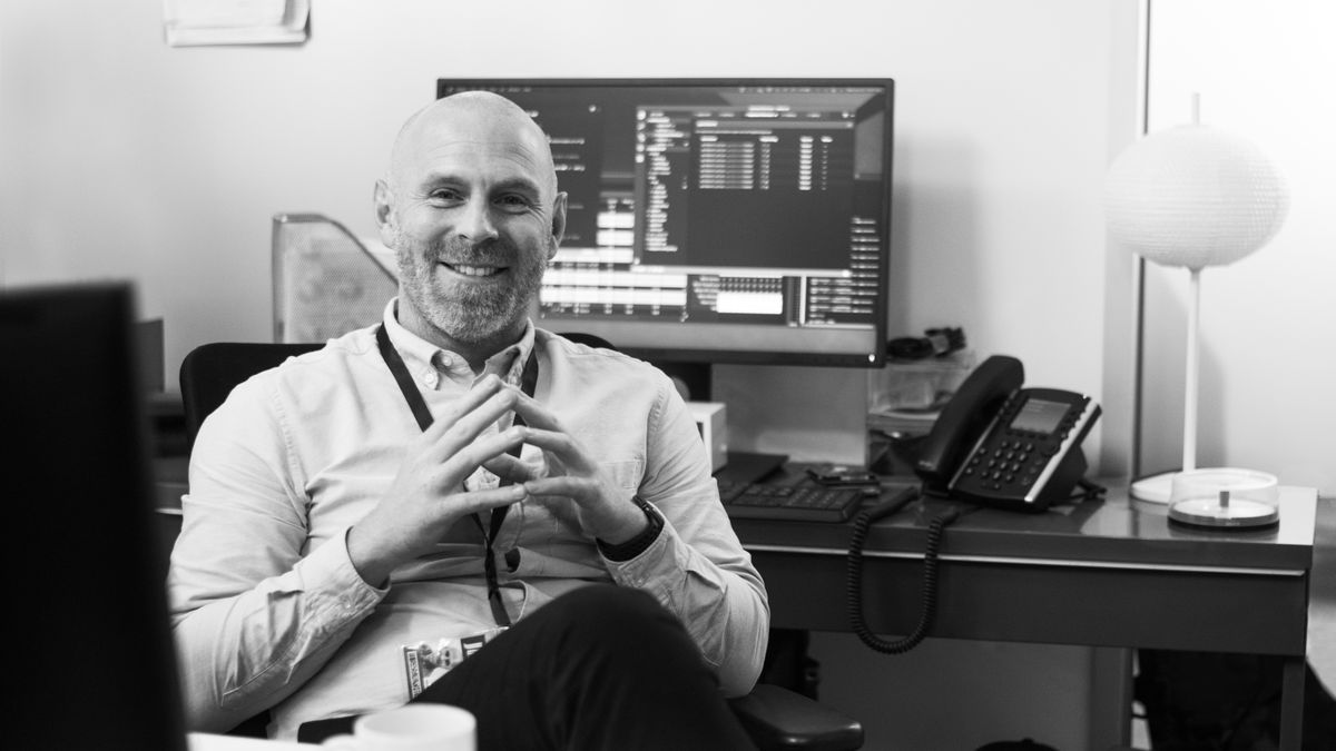 Office employee smiling sitting at his desk with computer monitor in the background