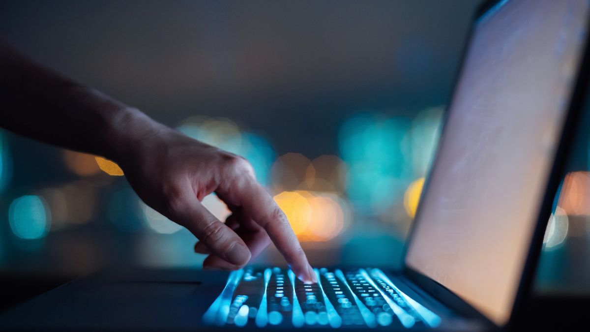 A human hand types on an illuminated keyboard in a dark room