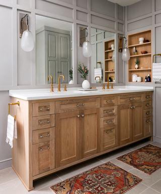 A bathroom with grey walls and wooden double vanity with brass taps and marble worktop