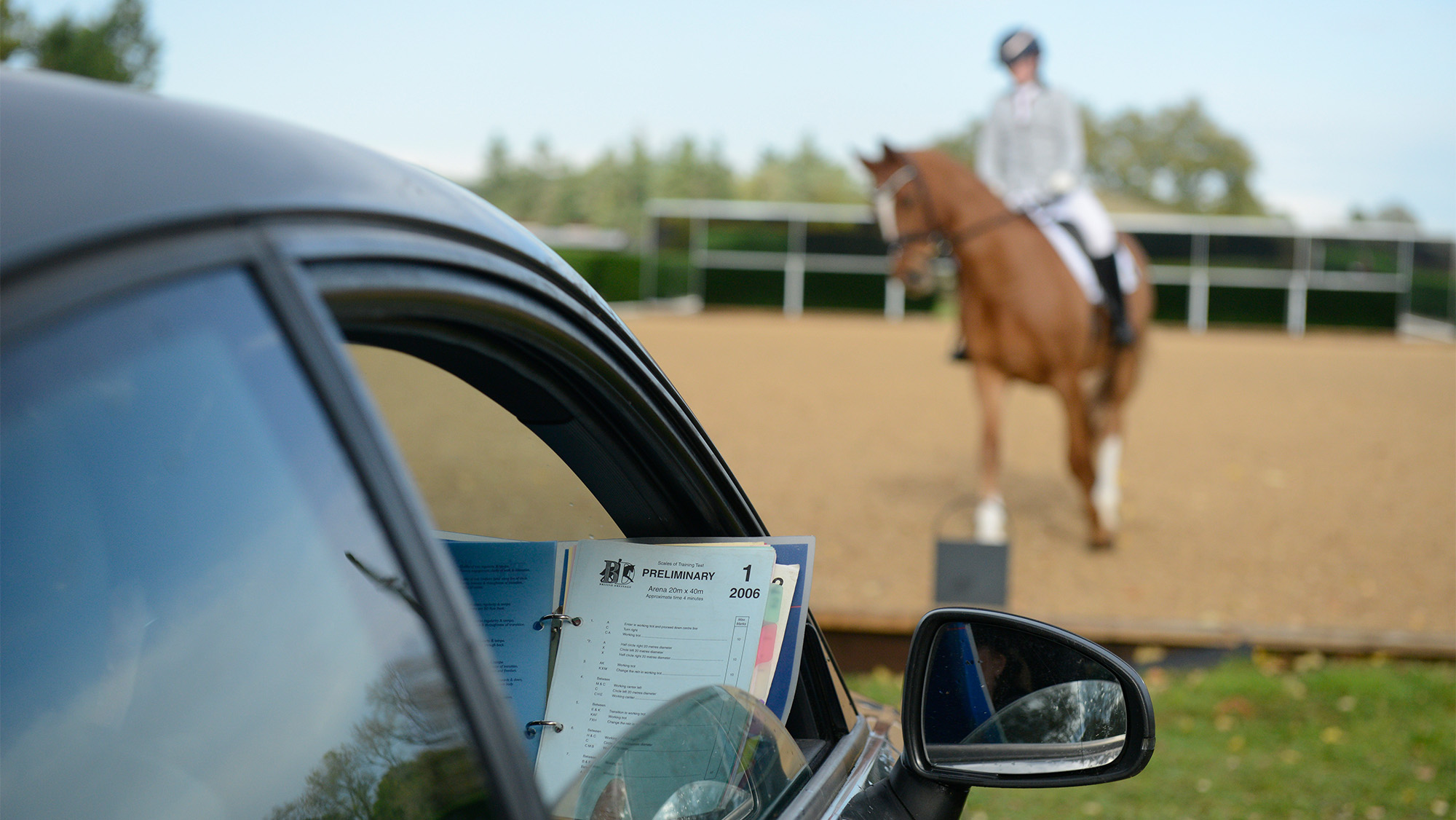 Dressage judge&amp;rsquo;s car with rider and horse riding test in the background