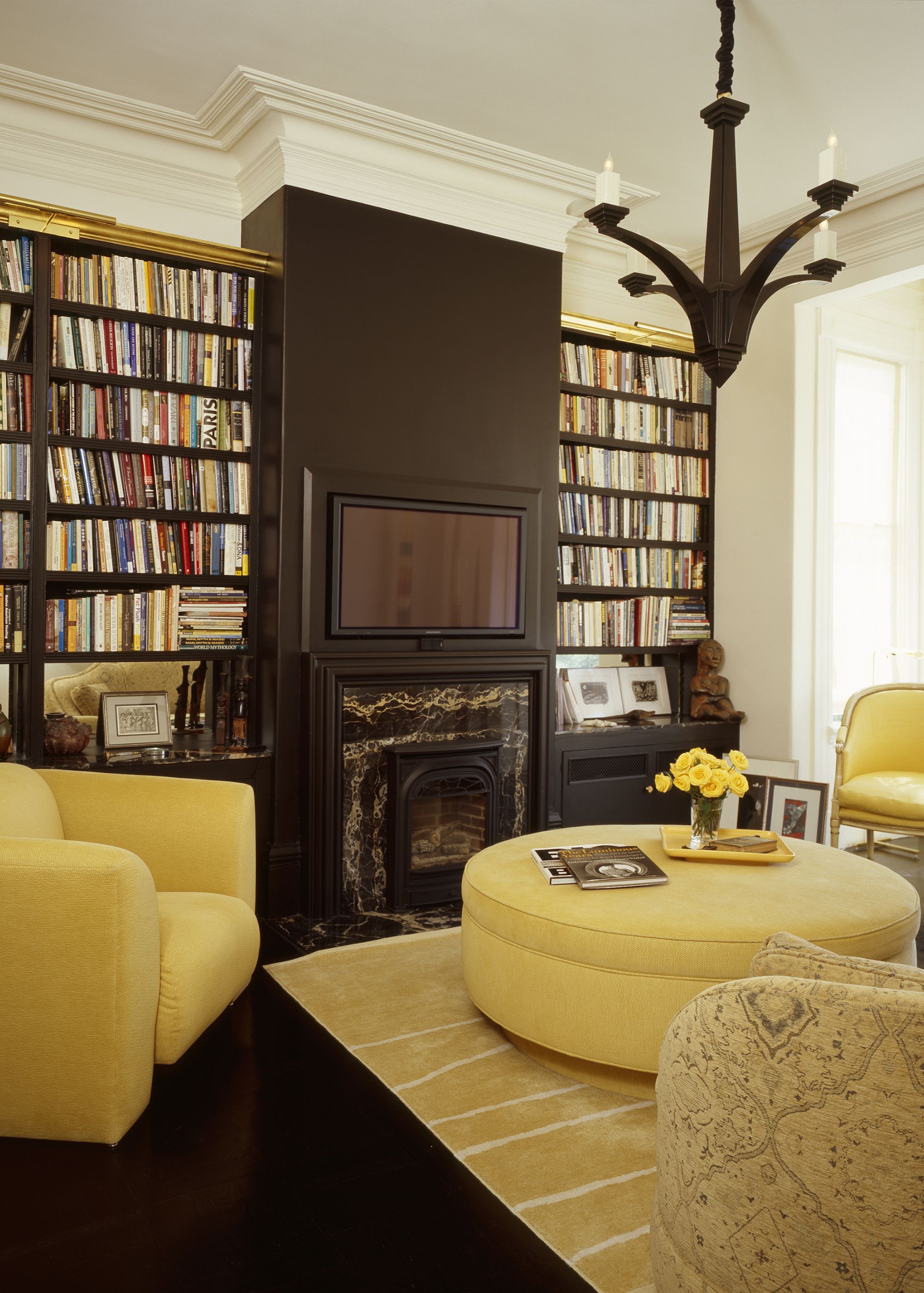 A living room with yellow furniture, black painted walls, and books along with a tv and fireplace