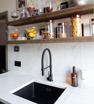 kitchen sink area with white wall tiles and wooden shelves