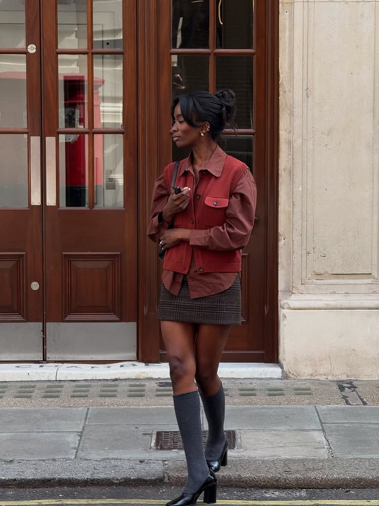 @_livmadeline wears a rust shirt, matching knitted vest, checked skirt and knee boots