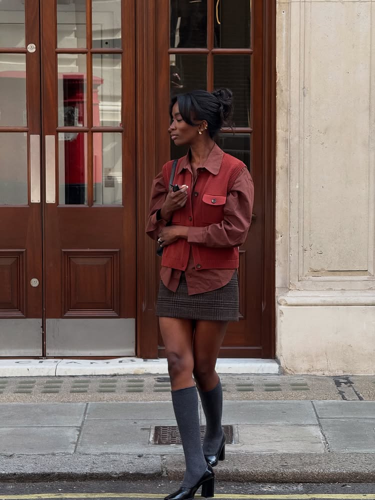 @_livmadeline wears a rust shirt, matching knitted vest, checked skirt and knee boots