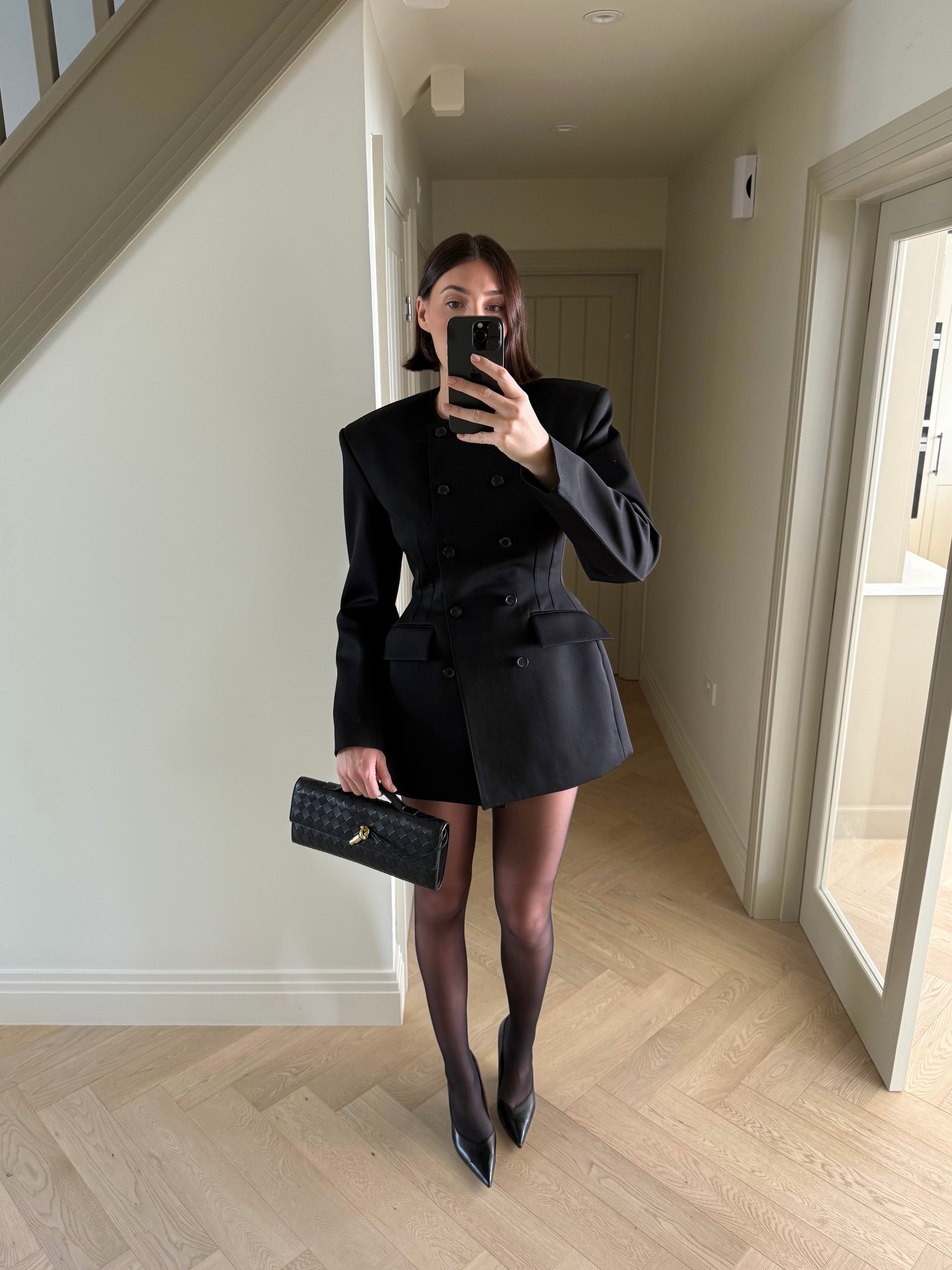 Influencer @sarahlouiseblythe takes a mirror selfie wearing a black Wardrobe.NYC blazer dress with tights and pointed-toe heels.