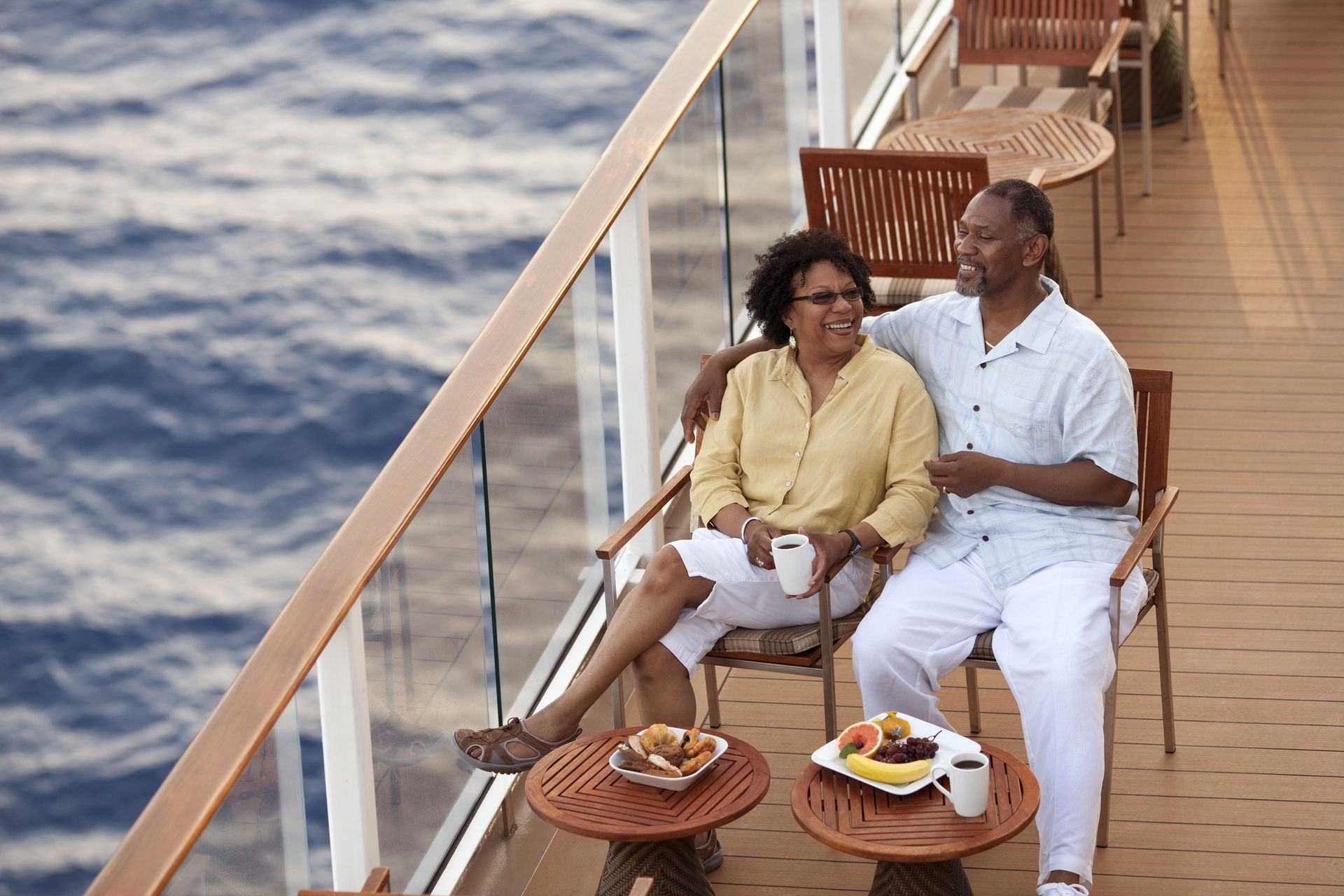 A mature couple lounging on board a cruise ship with breakfast on a table in front of them.