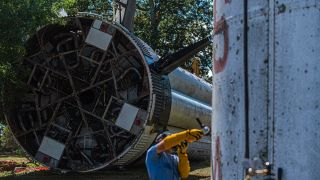 a person in a hardhat runs an angle grinder down the side of a giant rocket booster