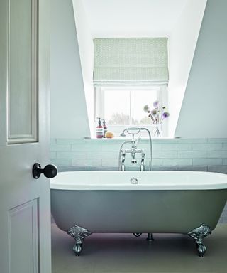 white bathroom with gray roll top tub, white backsplash and gray and white roman blind