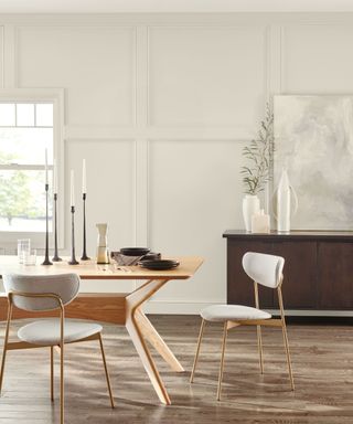 dining room with light gray panelled walls, wooden sideboard and light wood dining table with two chairs