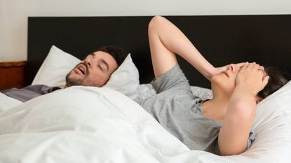 Man and woman in bed with woman annoyed by her partners' snoring, sleep & wellness tips