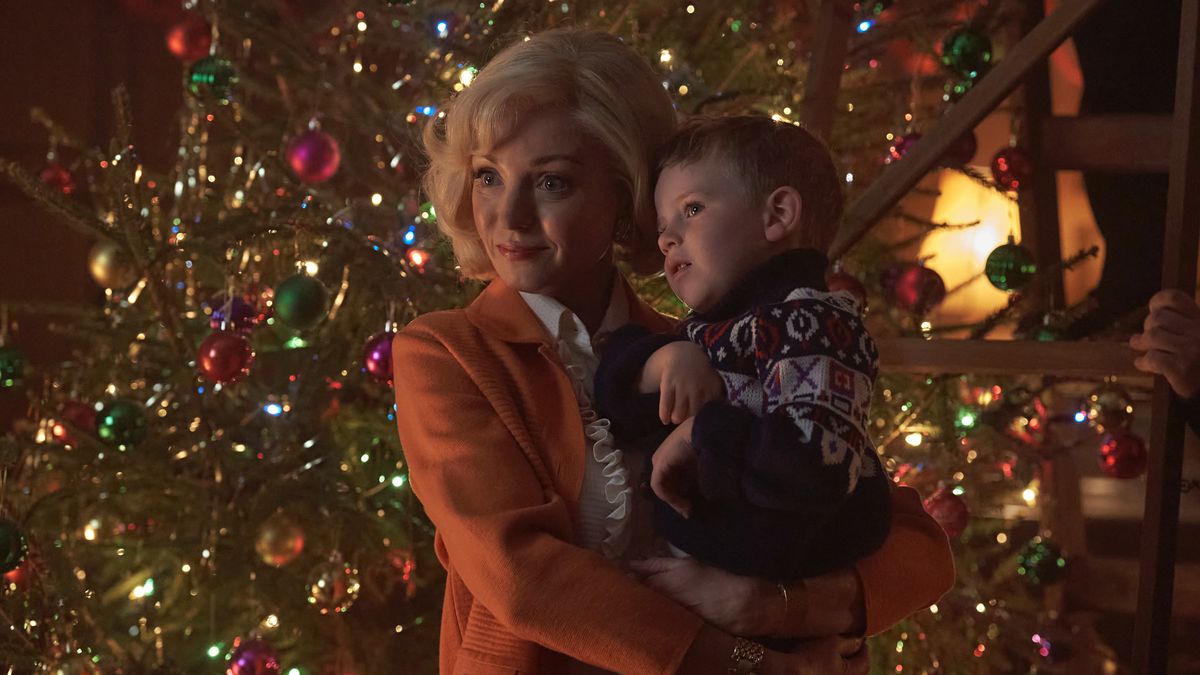 Helen George as Trixie in an orange jacket holds Archie O&#039;Callaghan as Jonty wearing a festive jumper in front of a Christmas tree in Call the Midwife.