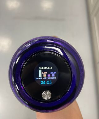 Close up of the Dyson V15 Detect screen displaying 104 million vacuumed particles and 24 minutes remaining battery life in Future test center