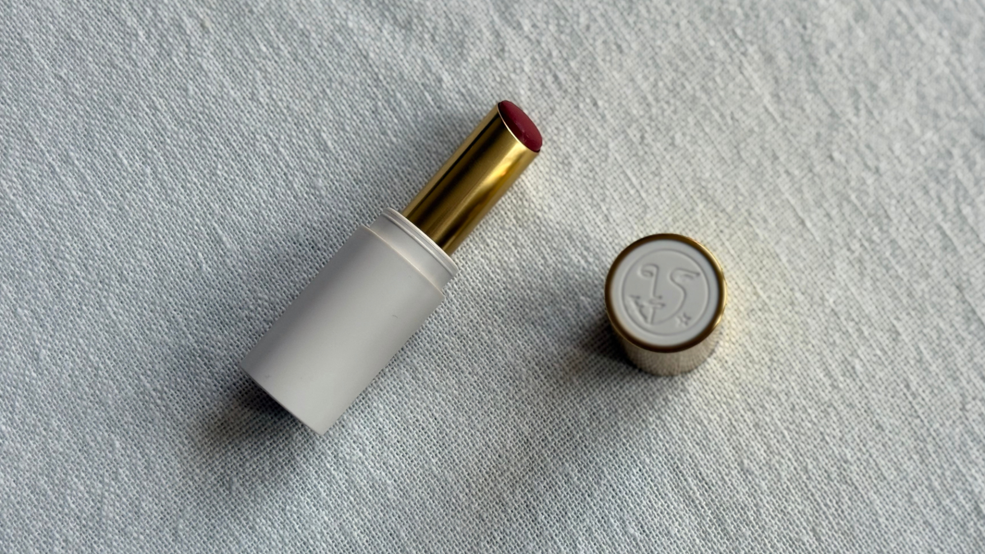 A birds eye view image of the Violette FR Bisou Balm in the shade Mon Cheri with the cap off, laying on an off-white linen background