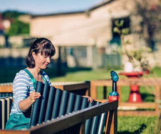 A woman uses a drill to construct a metal raised garden bed