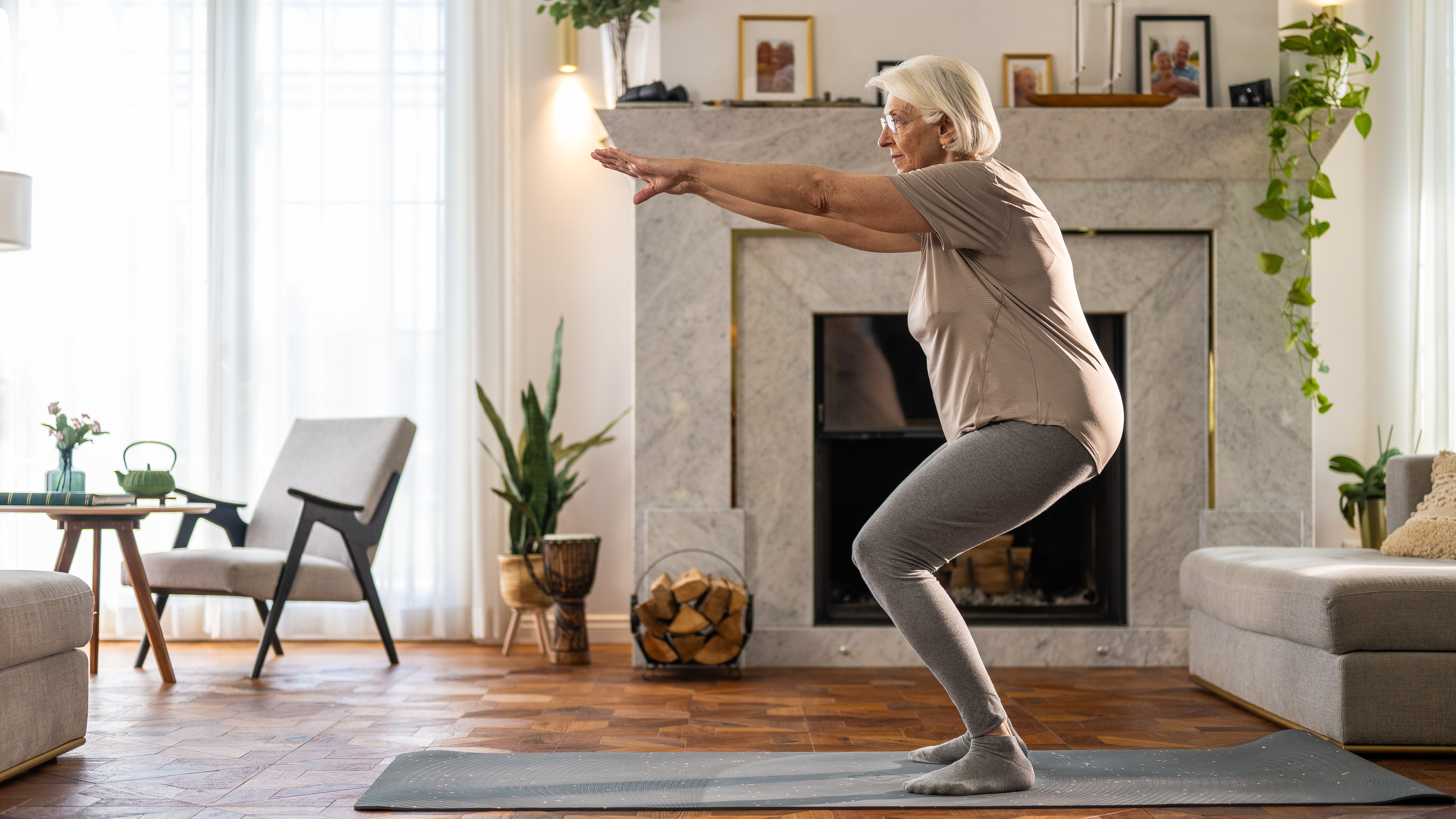 A woman performs shallow squats on an exercise mat in a living room.