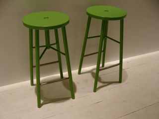 2 green high stools with round seats and 4 legs photographed against a white wall and white floors