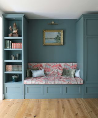 A built-in banquette with bold coral-patterned cushions sits snugly in a teal alcove, flanked by matching cabinetry.