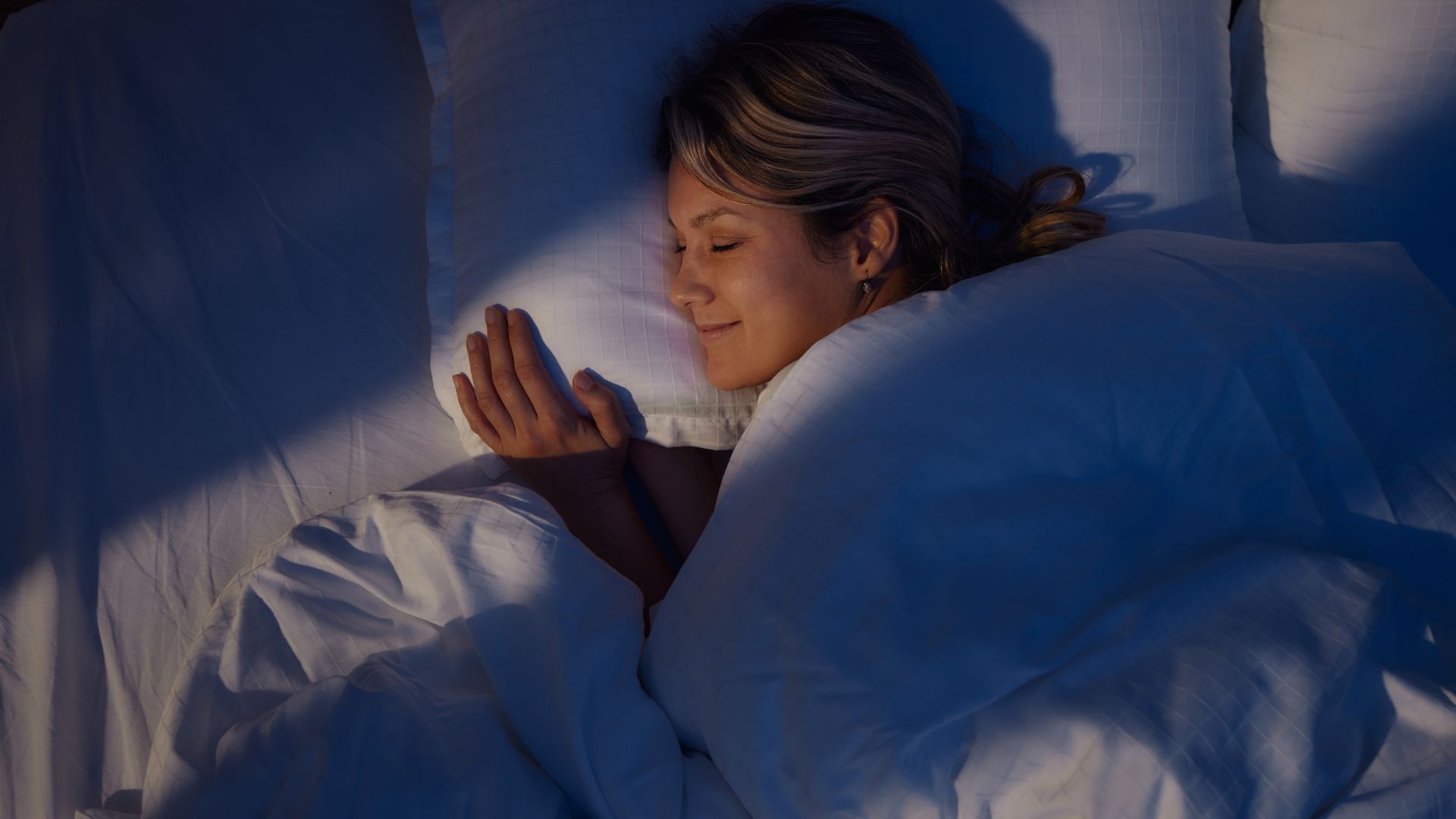 A woman smiling as she sleeps on her side with her head resting on a pillow.