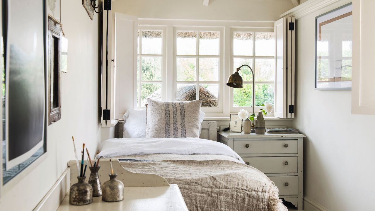 Small bedroom with pale cream walls, single bed with brown bedding, framed pictures on the walls and wooden vaulted ceiling