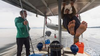 Alex Honnold does pull ups on a sail boat in Alaska's Inside Passage as Tommy Caldwell looks on.