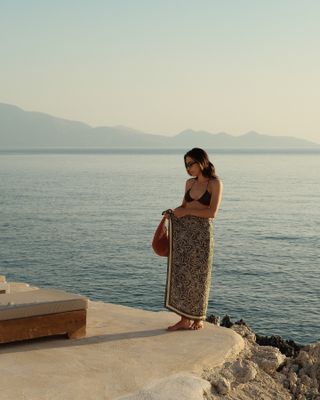 Woman by sea wears brown bikini top and sarong