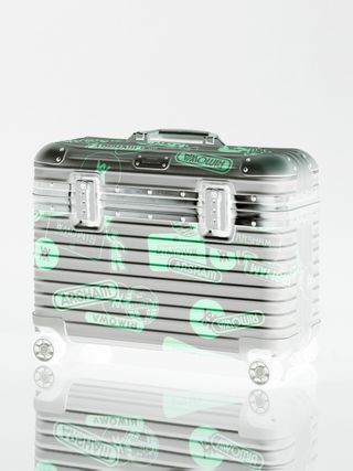 A grey suitcase covered in Assrham and Riwona labels.
