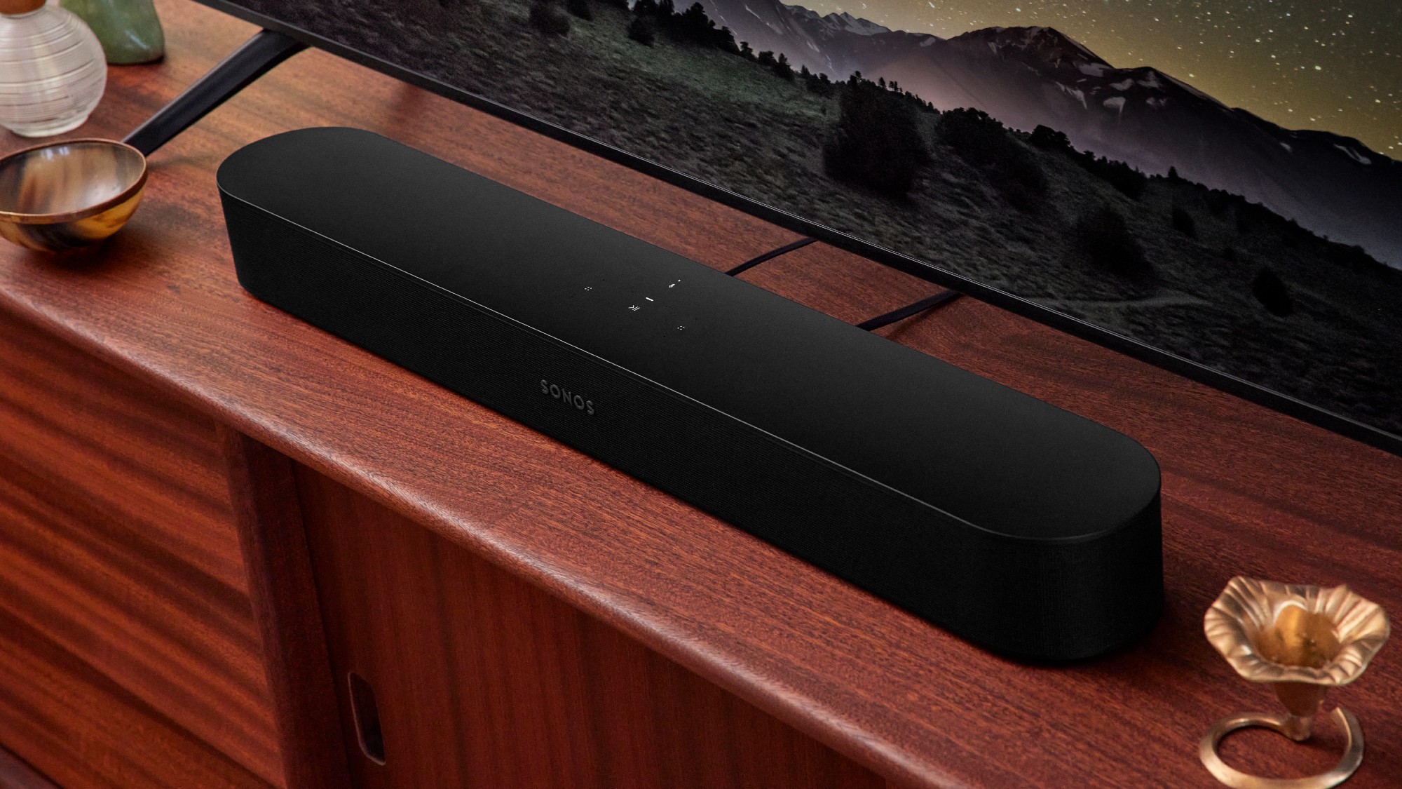 A Sonos Bean 2 in front of a television and sitting on a shelf. 