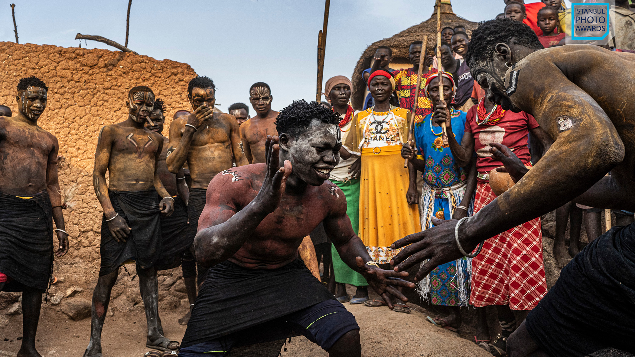 Two tribesmen wrestle each other surrounded by a crowd.