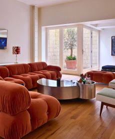 Basement living room with hardwood floors, orange velvet cloud sofas, mid century chairs and small enclosed courtyard at far back with potted tree