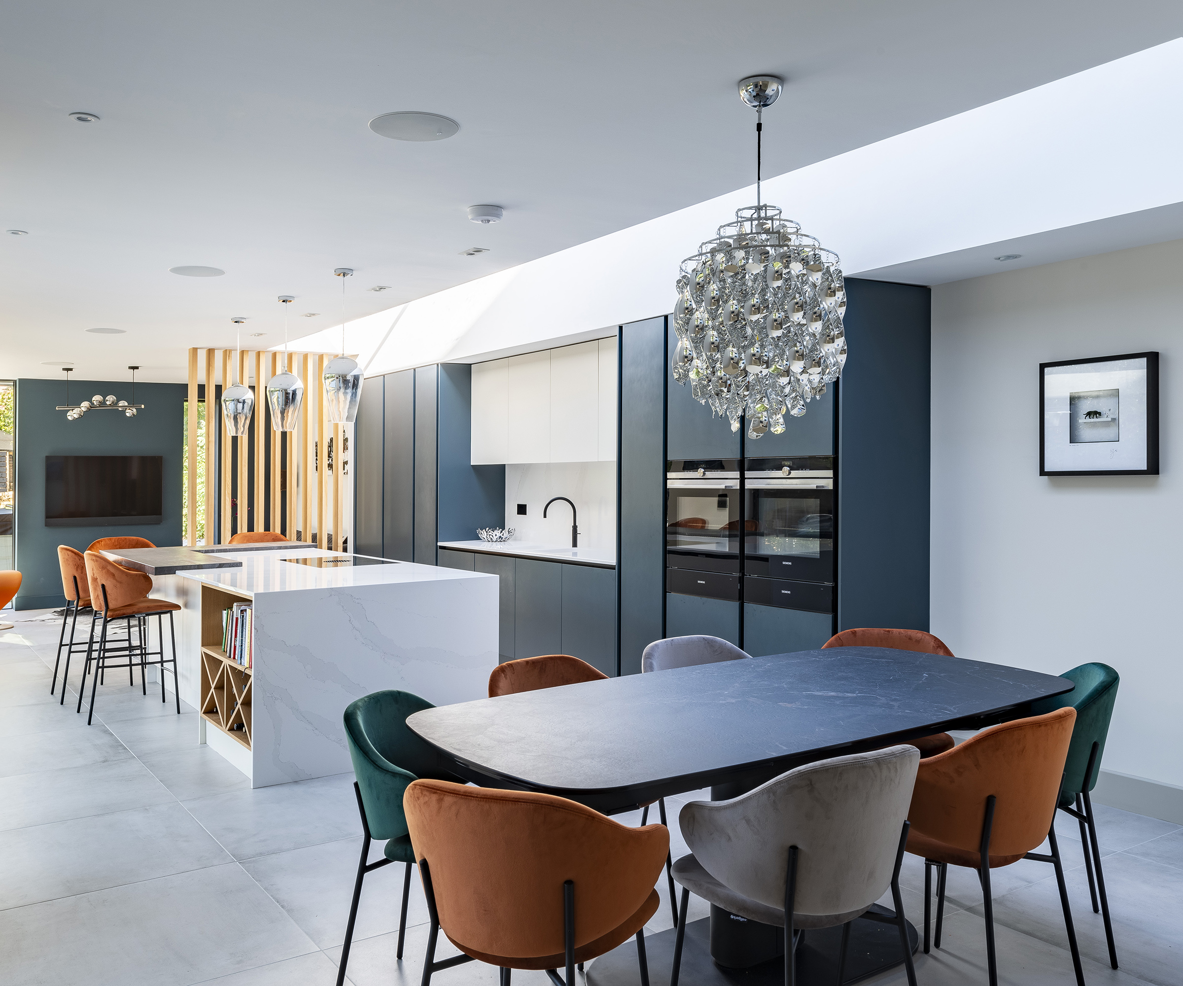 a modern kitchen dining room with teal and white decor and orange furniture. There is roof glazing casting natural light in the space