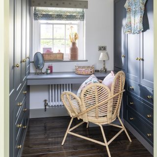 Dressing table and built in storage in a bedroom with rattan chair.