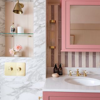 bathroom sink next to marble tiled wall, underneath striped splashback and pink bathroom cabinet