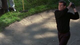 Pierce Brosnan in all black taking a golf shot