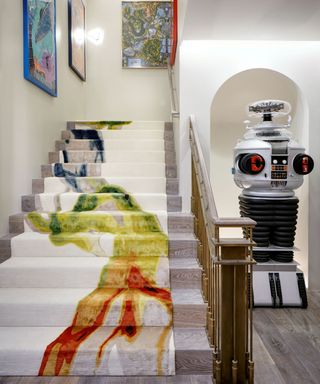 staircase with colorful rug runner and robot in alcove and artwork