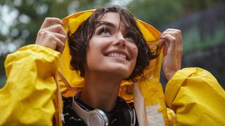A woman wearing a yellow raincoat putting her hood up in the rain