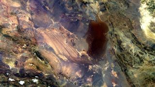 A false-color satellite image of a desert with a patch of parallel lines and a large shadowy patch