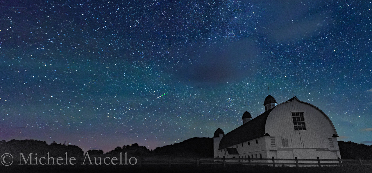 Uma chuva de meteoros é retratada contra um céu estrelado e um primeiro plano cênico