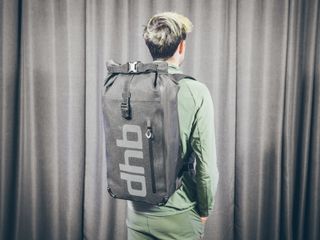 Will Jones, wearing the DHB Waterproof Rucksack, one of the best backpacks for cycling, stands in front of a wall